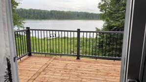 Een houten terras met een metalen hekwerk met uitzicht op een meer en bos.