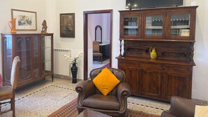 A living room with a brown leather armchair, a wooden cabinet with glass doors, a television on top, and a radiator. - Historical Maison des Artistes in Aristocratic XVI Century Palace  (Napoli)