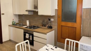A compact kitchen with white cabinets, a gas stove, a sink, and a wooden door with a frosted glass panel. - Historical Maison des Artistes in Aristocratic XVI Century Palace  (Napoli)