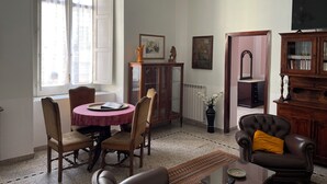 A living room with a dining table, chairs, a sofa, a television, and a cabinet. - Historical Maison des Artistes in Aristocratic XVI Century Palace  (Napoli)