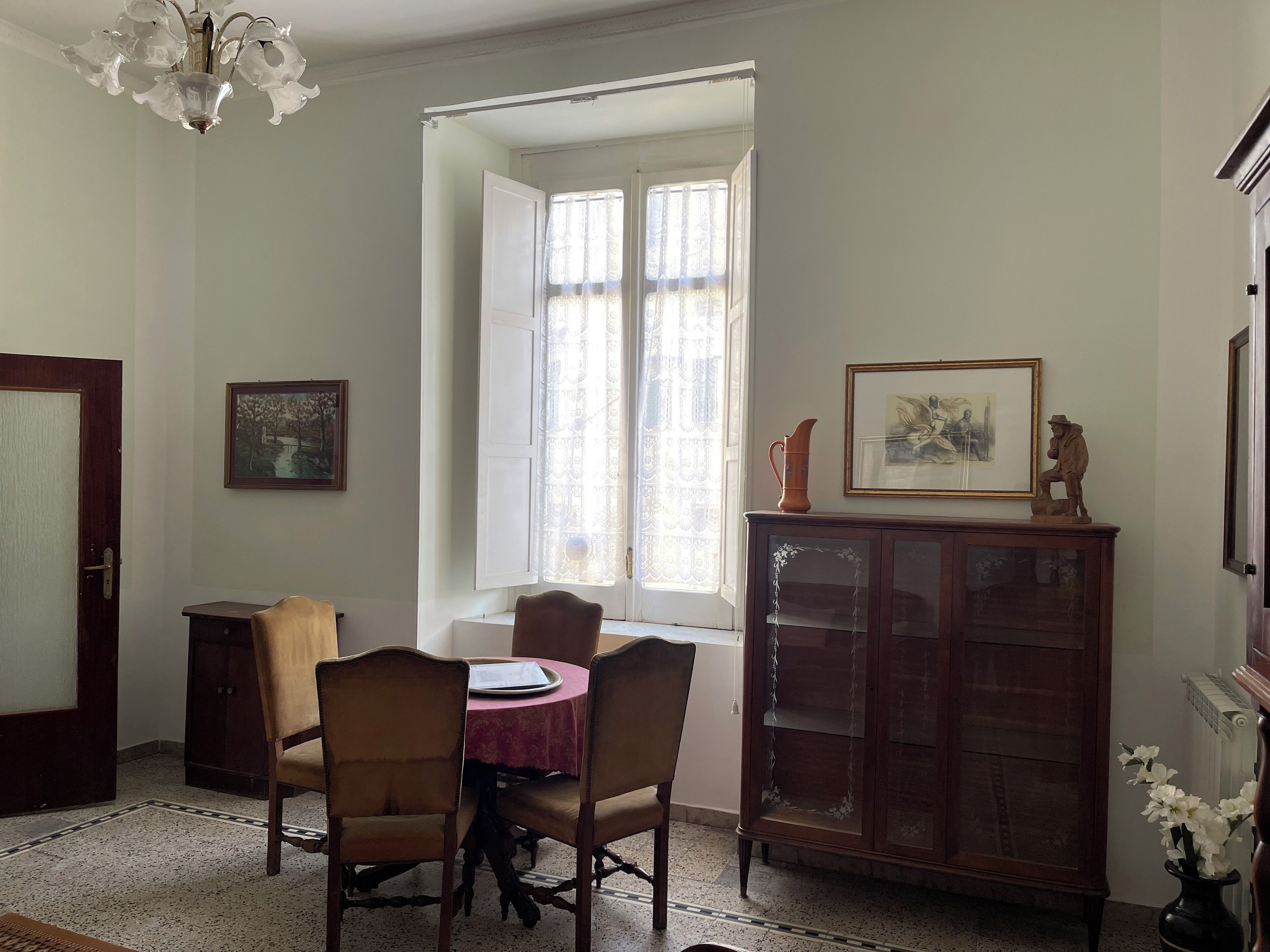 A dining area with a round table, chairs, a cabinet, and a window with curtains.