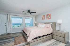A bedroom with a bed, a ceiling fan, a nightstand, a window with curtains, and artwork on the wall. - Beachfront 3BR Townhouse Not a Condo! Pet Friendly (Panama City Beach)