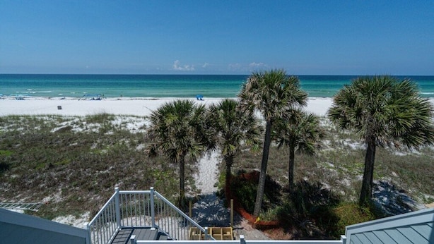 Blick auf einen Strand von einem Balkon, mit Palmen und blauem Himmel.