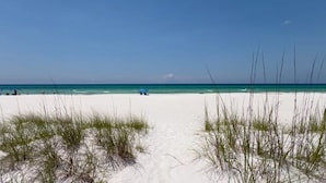 Ein Strand mit weißem Sand, klarem türkisblauem Wasser und spärlicher Vegetation.