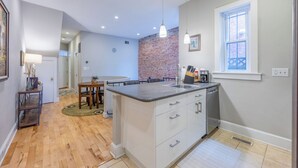 A modern kitchen with a central island, white cabinetry, and a brick accent wall.