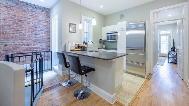 A modern kitchen with a central island, stainless steel appliances, and a brick accent wall.