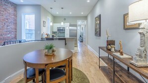 A modern kitchen with a dining area, featuring a brick wall, wooden flooring, and a view to the backyard.