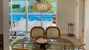 A dining area with a glass table and chairs, a wicker pendant light, and a sign above reading "EAT".