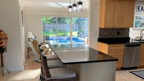 A spacious kitchen with a large island, wooden cabinets, and a view of a backyard with a pool.