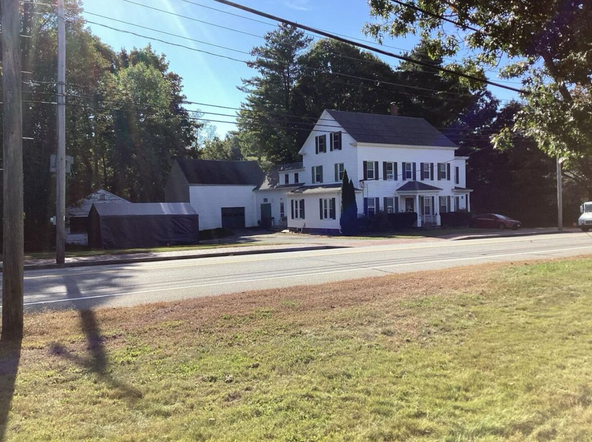 A two-story white house with a porch, located at the end of a street.