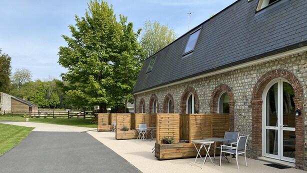 A building with a stone facade, arched windows, and a paved patio area with outdoor seating. - Aux Ecuries du Château  (Contremoulins)