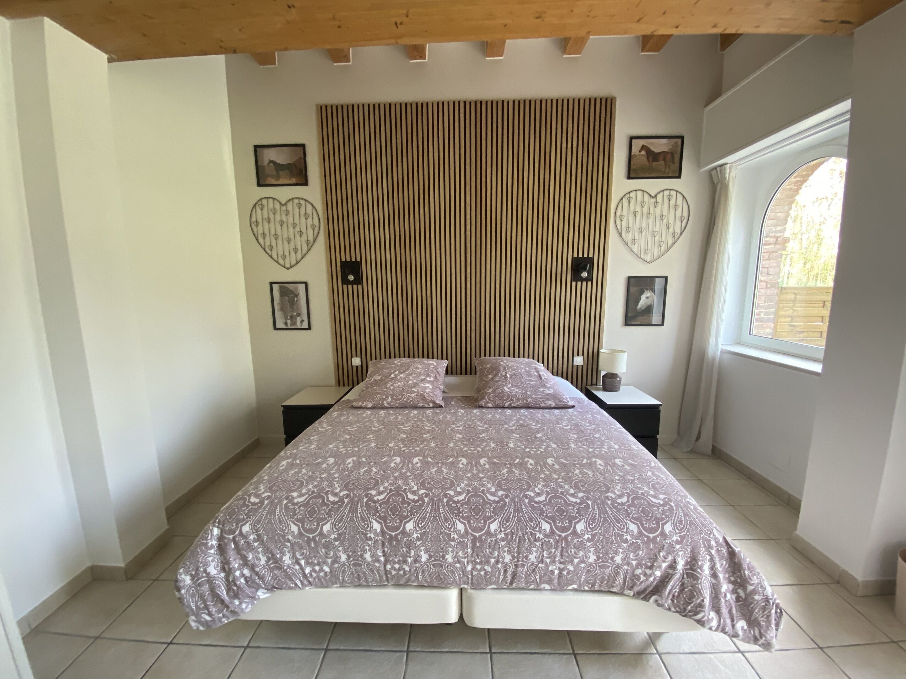 Un dormitorio con cama, dos mesitas de noche, una ventana y techo de madera.