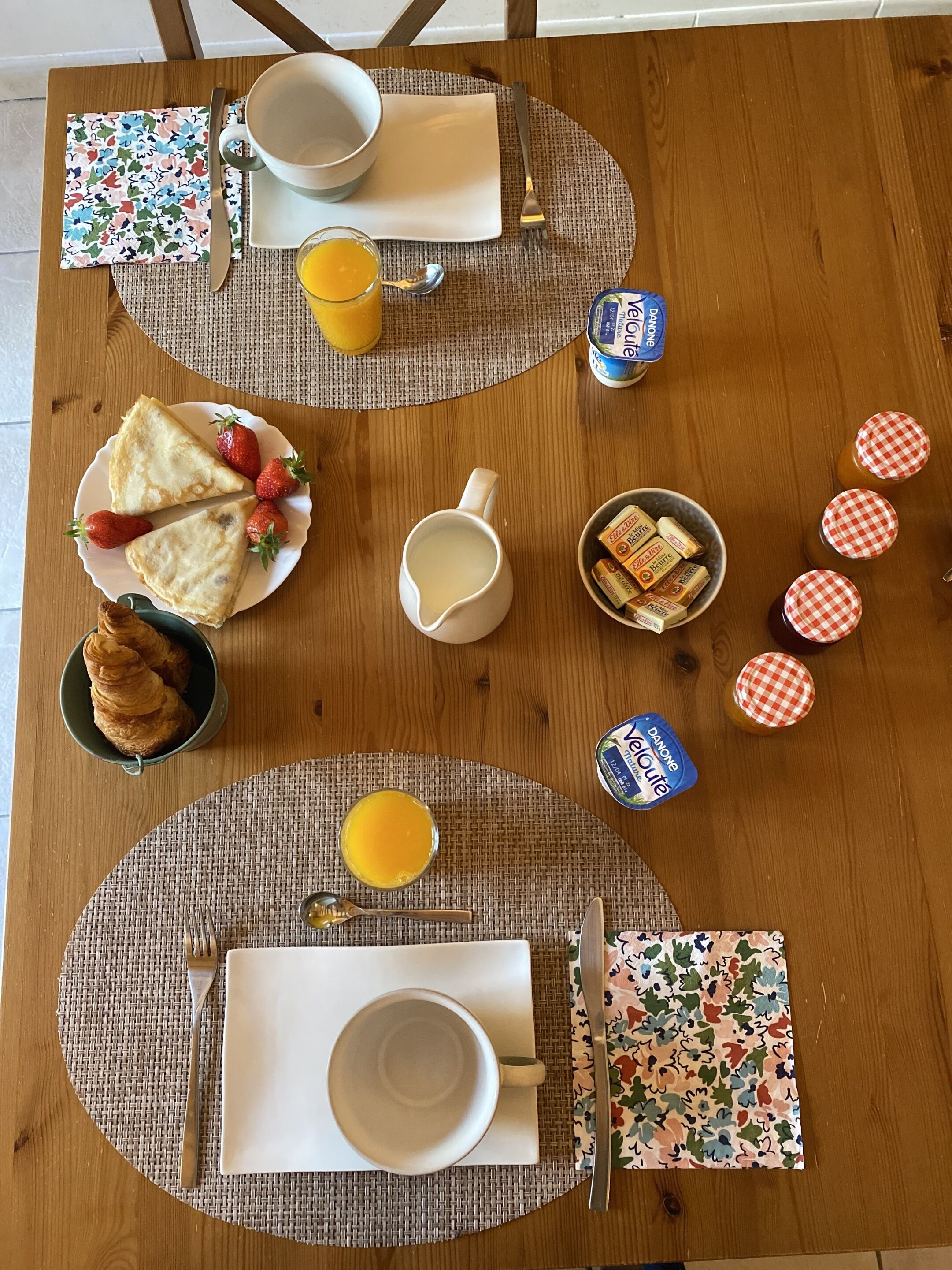 Mesa de café da manhã com panquecas, morangos, um pote de iogurte e uma jarra de suco de laranja.