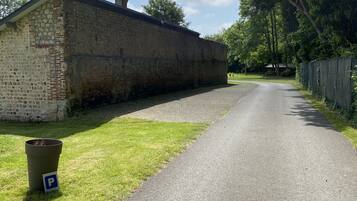 A narrow paved road flanked by a stone building and a green fence.