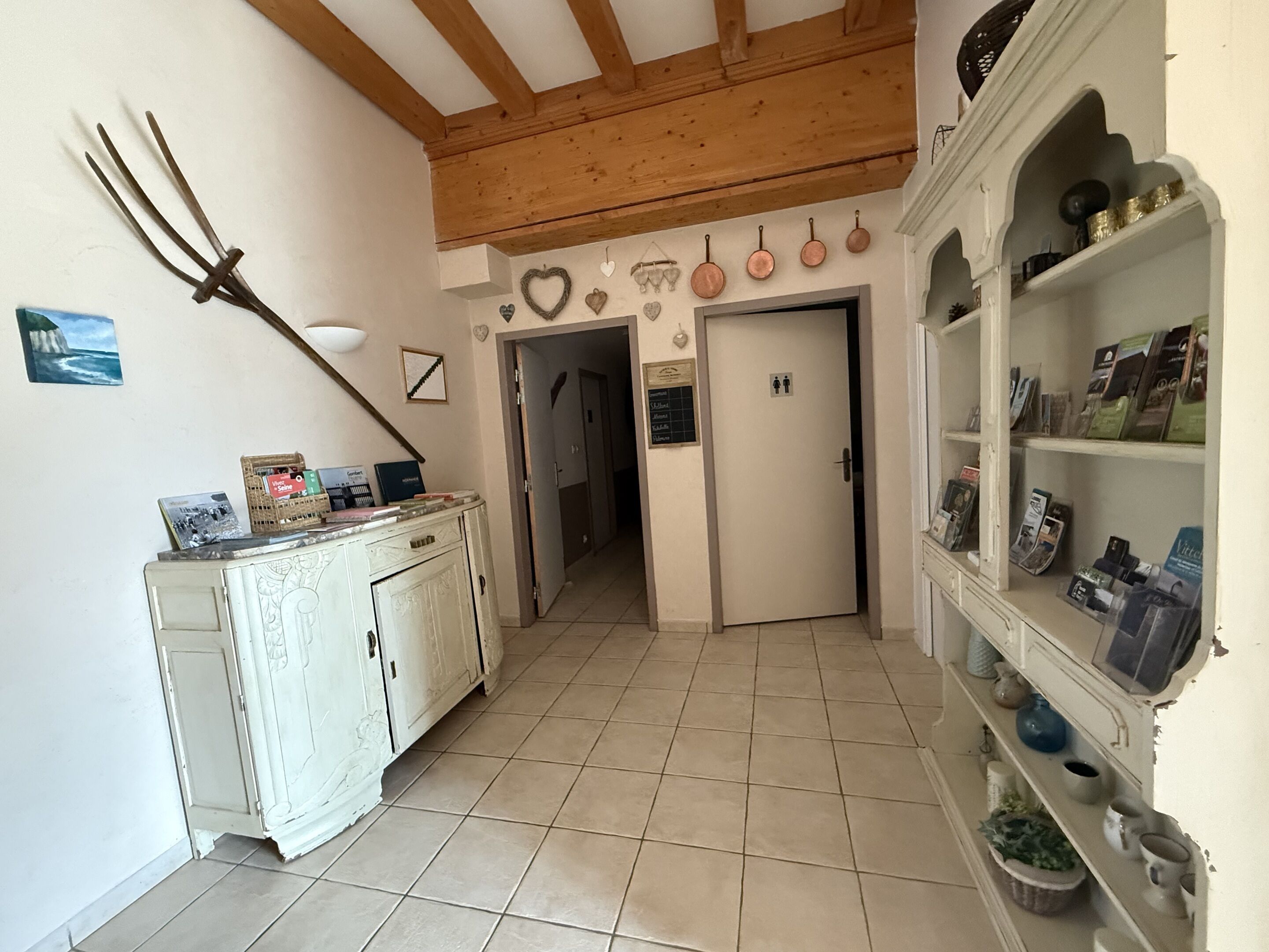 A hallway with a rustic wooden ceiling, a white door with a sign, and a shelf with various items.