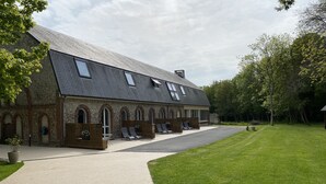 A building with a sloped roof and arched windows, a paved driveway, and a grassy lawn. - Aux Ecuries du Château  (Contremoulins)