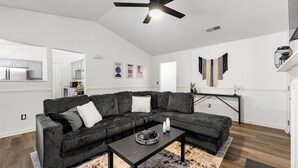 A modern living room with a sectional sofa, a coffee table, a ceiling fan, and a fireplace. - Charming 3BR 2BA Retreat: Cozy! (Decatur)