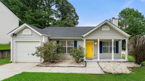 A single-story house with a garage, a front porch, and a yellow door. - Charming 3BR 2BA Retreat: Cozy! (Decatur)