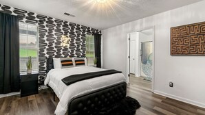 A bedroom with a bed, a black headboard, a white wall with a geometric pattern, a black and white striped pillow, and a black furry rug. - Charming 3BR 2BA Retreat: Cozy! (Decatur)