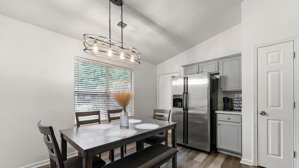 A modern kitchen with a dining table, chairs, and a bench. There is a refrigerator, cabinets, and a window with blinds. - Charming 3BR 2BA Retreat: Cozy! (Decatur)