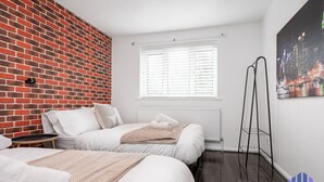 A hotel room with two beds, a brick wall, a window with blinds, and a cityscape painting. - Haven Noir by CEFAS - Pool Table - City & Man Utd (Greater Manchester)