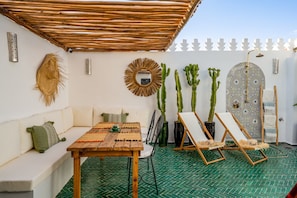 A cozy outdoor seating area with a woven ceiling, a round mirror, cacti, and a patterned wall.