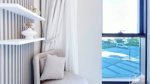 A modern room with a large window, a white chair, a white shelf with a vase, and a view of a parking lot outside. - Elegant 1B Apt&balcony in the Heart of Dubai Creek (Dubai)