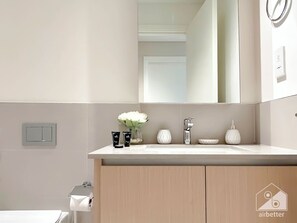 A modern bathroom with a white sink, a mirror, and a toilet. There are toiletries on the sink counter and a toilet paper holder on the wall. - Elegant 1B Apt&balcony in the Heart of Dubai Creek (Dubai)