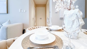 A dining area with a table set for two, featuring a white plate, a clear wine glass, and a vase with white flowers. - Elegant 1B Apt&balcony in the Heart of Dubai Creek (Dubai)