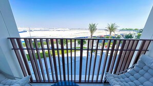 A balcony with a view of a beach and palm trees, two white cushioned chairs, and a small potted plant. - Elegant 1B Apt&balcony in the Heart of Dubai Creek (Dubai)