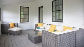 A covered outdoor seating area with wicker furniture and cushions, large windows, and a wooden deck. - Historic Charm & Modern Comfort, Beach Vacation Awaits. (Wells)