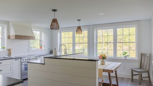 A kitchen with white cabinetry, a central island, a built-in oven, and large windows offering a view of greenery outside. - Historic Charm & Modern Comfort, Beach Vacation Awaits. (Wells)