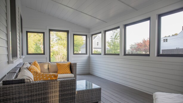 A covered porch with wicker furniture, large windows, and a view of trees and a house. - Historic Charm & Modern Comfort, Beach Vacation Awaits. (Wells)