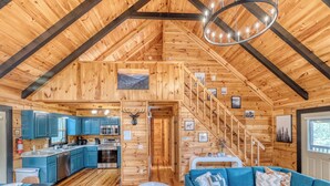 A log cabin with a kitchen, dining area, and living room, featuring wooden walls and a staircase. - SPECIAL -  Make Your Labor Day a Mountain Getaway. Hot Tub, Fire Pit, Games (Mineral Bluff)