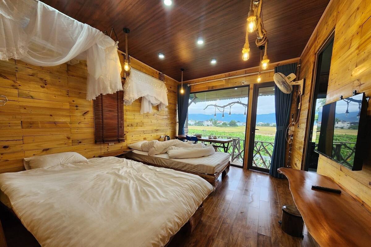 Een houten slaapkamer met twee bedden, een tafel en uitzicht op het landschap.