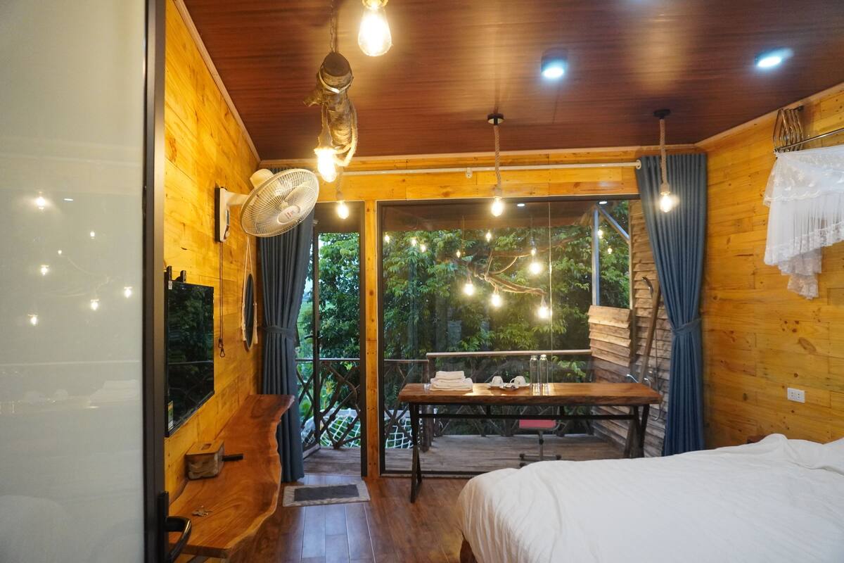 Een houten hutje met een bed, een tafel en een balkon met uitzicht op het bos.