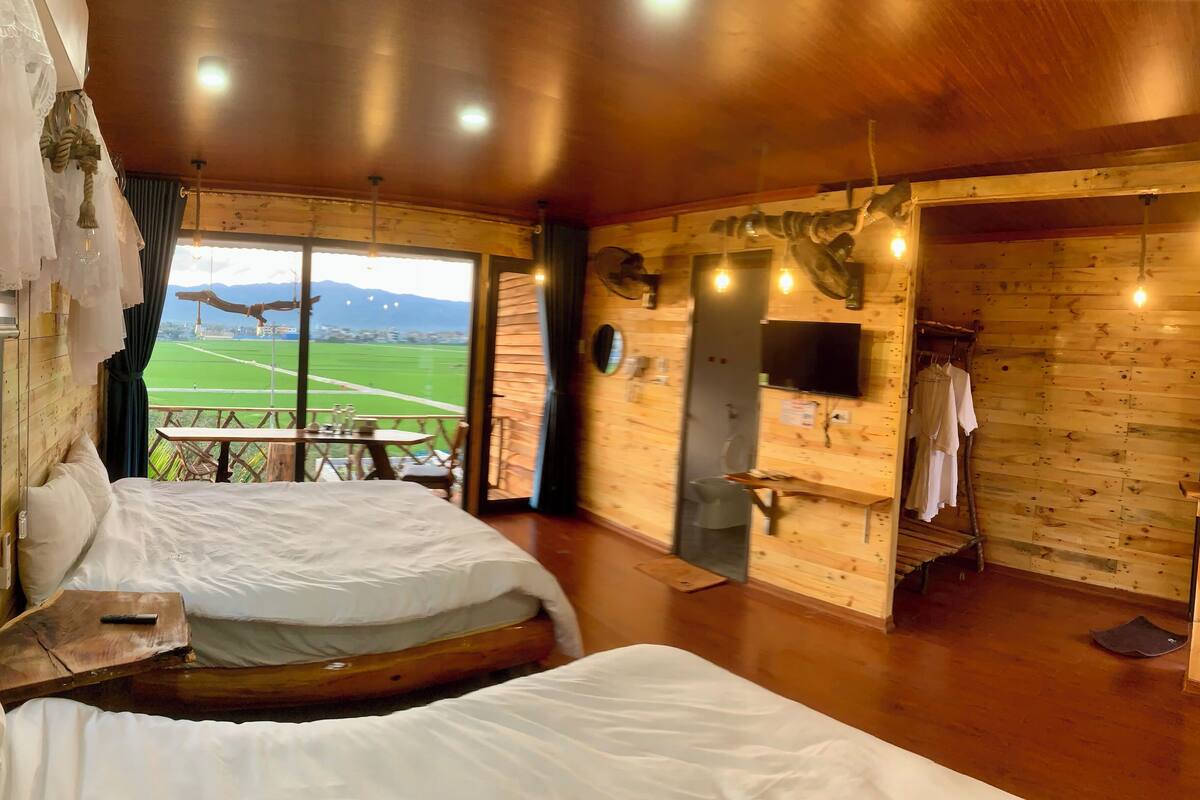 Een houten kamer met twee bedden, een televisie en uitzicht op een groen veld.