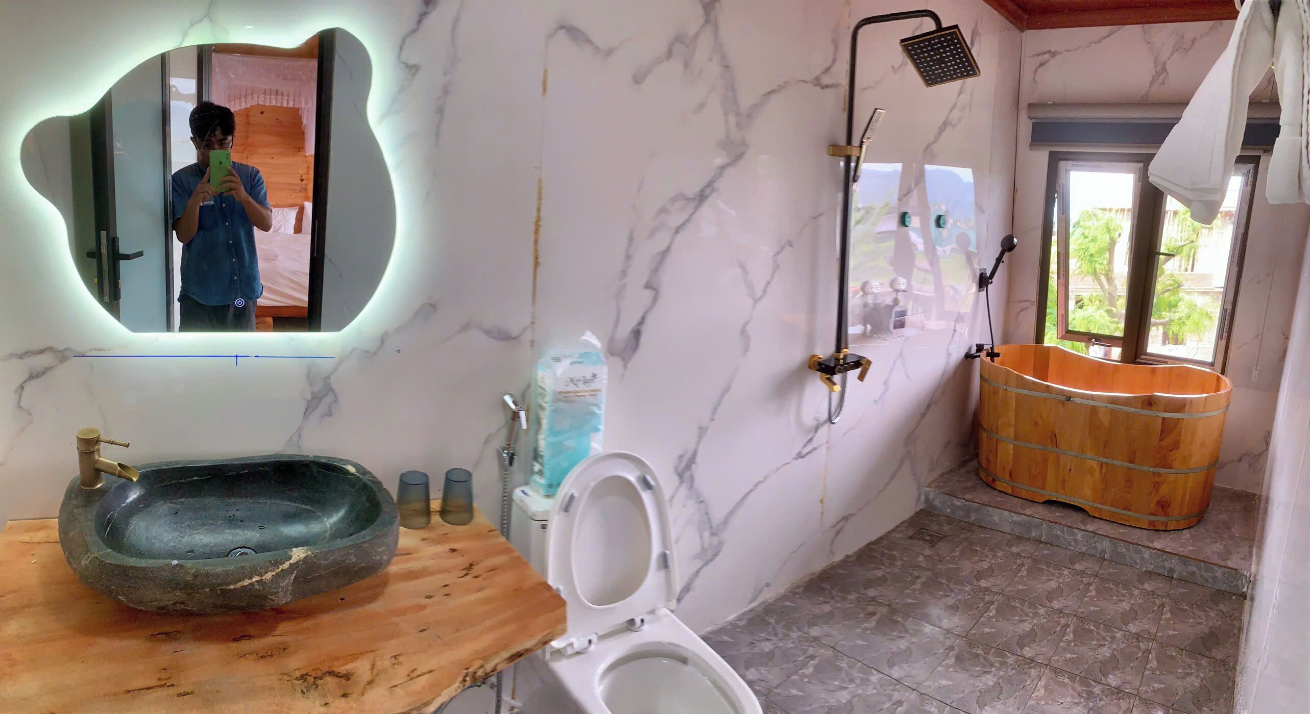 Un baño con pared de mármol, lavabo de madera, inodoro, ducha y bañera de madera.