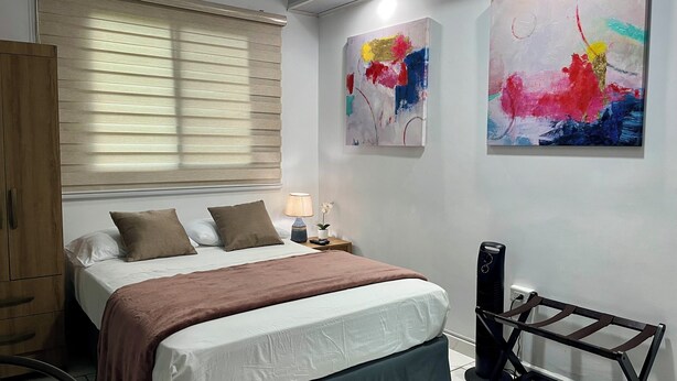 Une chambre à coucher avec un lit, des oreillers, une table de chevet avec une lampe, une petite table ornée d’une orchidée et des tableaux abstraits accrochés au mur.