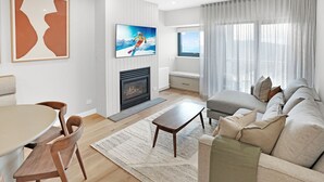 A modern living room with a fireplace, a sofa, a TV, and a dining area. - Alto 502 - Mount Buller Apartment (Mount Buller)
