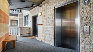 An elevator with a metallic finish, adjacent to a wall with a textured stone pattern. - Alto 502 - Mount Buller Apartment (Mount Buller)