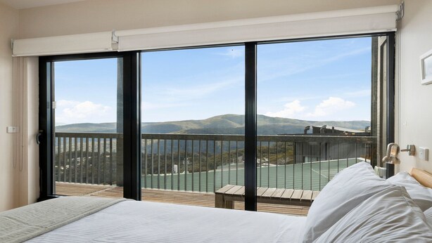 A bedroom with a large window, a bed, and a view of a mountainous landscape. - Alto 502 - Mount Buller Apartment (Mount Buller)