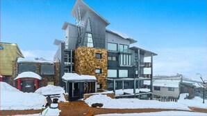 A modern multi-story building with a stone facade, large windows, and a sloped roof. - Alto 502 - Mount Buller Apartment (Mount Buller)