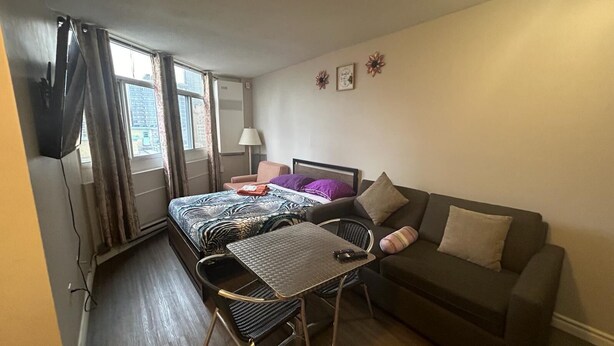 Una habitación de hotel compacta con una cama, un sofá, una mesita y una silla.