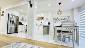 Una cocina moderna con armarios blancos, un refrigerador de acero inoxidable y un comedor con mesa y sillas de madera.