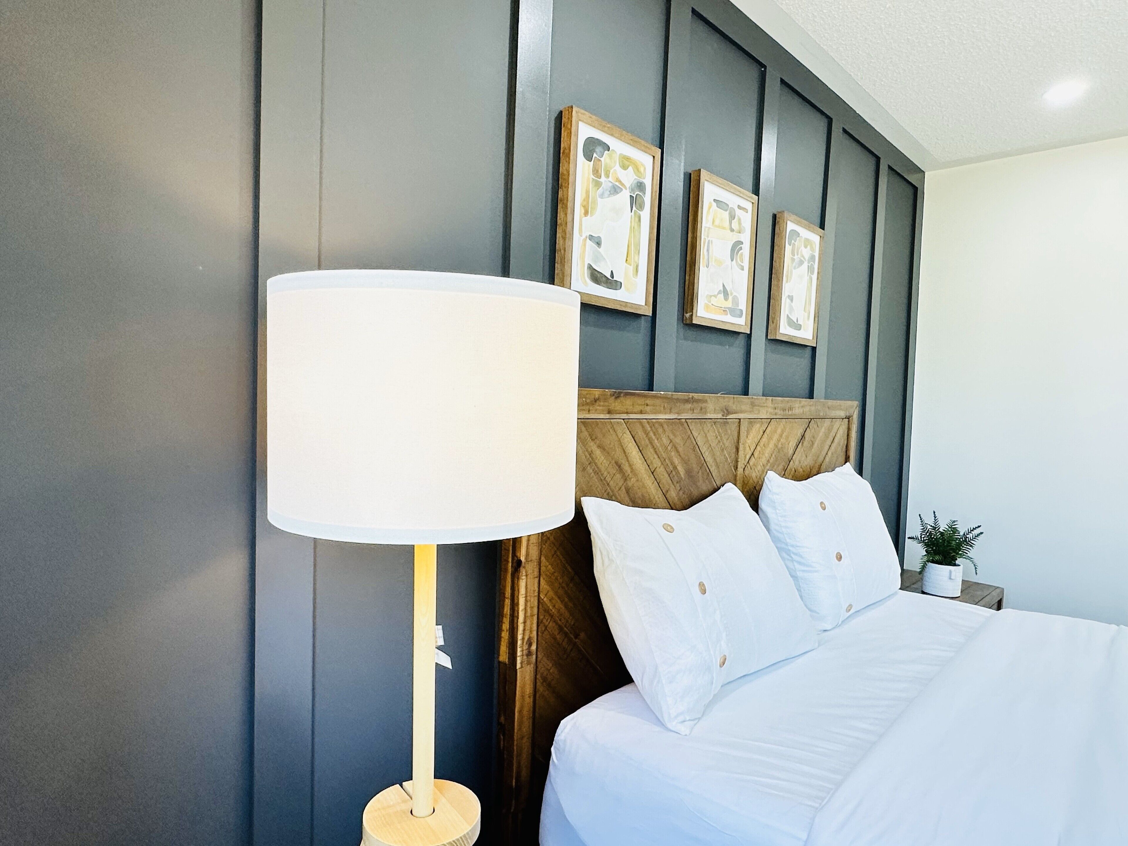 Quarto de hotel com cama, mesa de cabeceira, abajur e obras de arte emolduradas na parede.