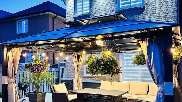 Un patio cubierto con mobiliario exterior, luces colgantes y una planta en maceta.