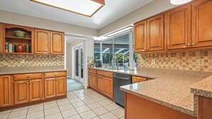 A kitchen with wooden cabinets, granite countertops, and a dishwasher. - Lake Front! Spacious Home w/heated pool & kayaks (Lake Wales)