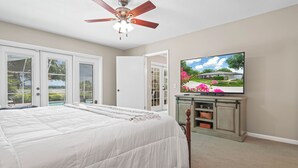 A bedroom with a bed, a ceiling fan, a television on a stand, and a sliding glass door leading to a balcony. - Lake Front! Spacious Home w/heated pool & kayaks (Lake Wales)