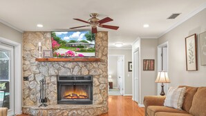 A living room with a stone fireplace, a ceiling fan, and a television mounted above it. - Lake Front! Spacious Home w/heated pool & kayaks (Lake Wales)